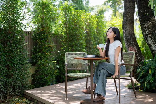 Asian Woman Holding Coffee Cup Looking Peaceful on Garden Patio