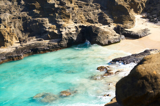 Rocky cliffs and sandy beach with ocean waves on oahu Hawaii coast