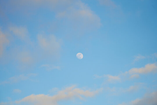 Daytime moon seen in blue sky with clouds over Oahu, Hawaii