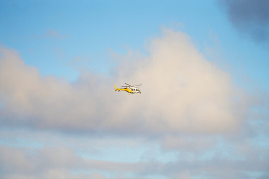Yellow helicopter flying in partly cloudy sky