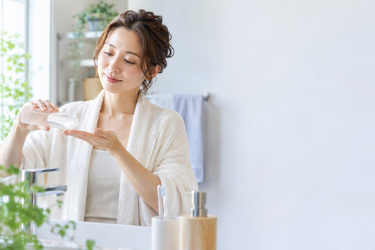 洗面所で笑顔で化粧水を手に取る女性