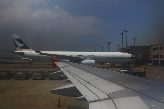Airplane wing view looking at Cathay Pacific airliner on tarmac.