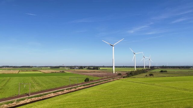 A passenger train of the Nederlandse Spoorwegen NS travels along wind turbines producing sustainable energy.