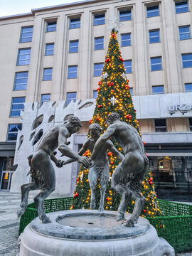 Gliwice, Poland - 31 December 2022: Old antique fountain with cast iron sculpture of three "Dancing Fauns", Christmas tree on city street. Little Devils statue by 1928 Hans Dammann scuptor