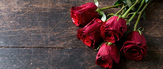 Fototapeta premium Five red roses with water droplets arranged on a dark wooden table