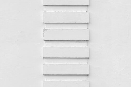 Minimal white plaster wall featuring a vertical column of rectangular reliefs, strong geometric pattern and subtle shadows. Clean architectural seamlestexture for backgrounds and design projects