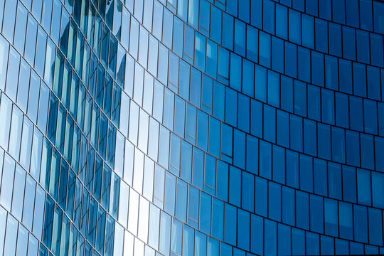 Curved blue glass facade creates abstract architecture where vertical rhythm and reflective surfaces follow the curved facade across blue glass surfaces