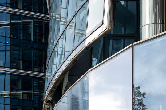 Curved metallic glass facade creates abstract architecture where surfaces reflections and urban geometry follow the curved glass facade across metallic surfaces