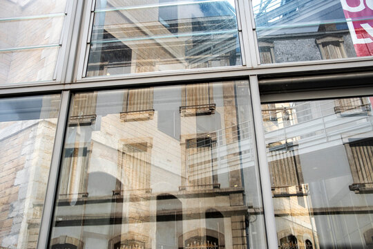 Reflections in a glass facade reveal older buildings and create abstract architecture where transparency layers and textures merge across the glass facade