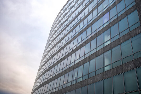 Curved glass facade creates abstract architecture with blue reflections and modern lines where perspective shapes the curved facade across blue glass