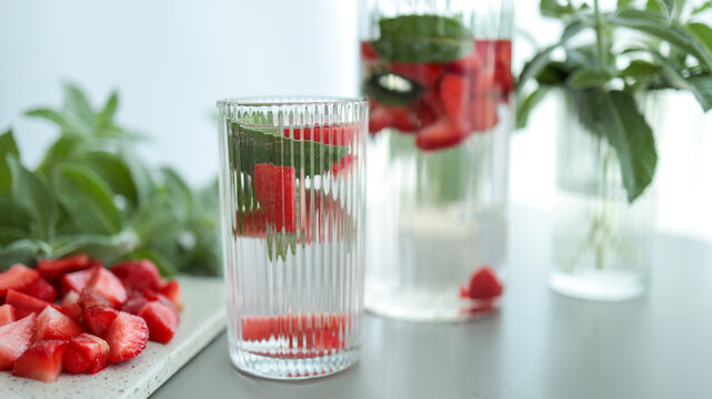 Row of glasses filled with ice fresh mint leaves and strawberries on light background. JPG