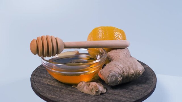 Lemon, sliced ginger and honey with a wooden dipper rotate on a stand against white. Traditional seasonal self care and comforting food ingredients concept