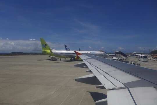 Airplane wing view on airport tarmac with parked passenger airliners.