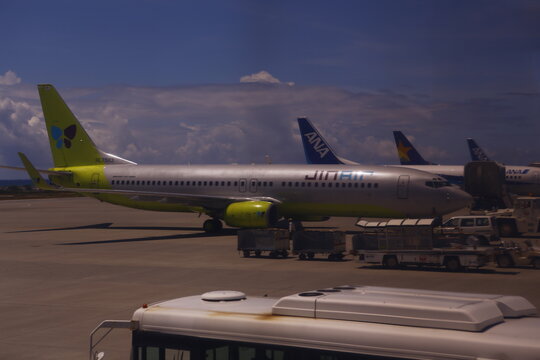 Jin Air passenger airliner parked on airport tarmac under cloudy blue sky.