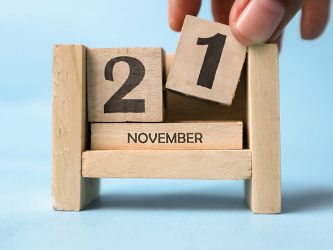 A woman's hand is holding a wooden block with the number 1 written on it on a wooden block calendar for November 21st on a light blue background.