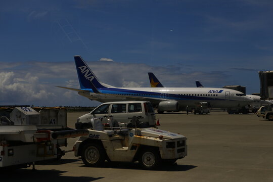 ANA passenger airplane parked on tarmac with airport ground support vehicles.