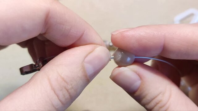Detailed assembly of natural sunstone gemstone beads threaded with silver components and metallic hardware on a neutral workspace surface