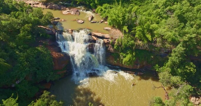 Drone view of Tat Huang Waterfall, the Thai Lao Friendship Waterfall, located in Na Haeo District, Loei. Surrounded by dense rainforest and mountains, this cross-border waterfall is a hidden gem