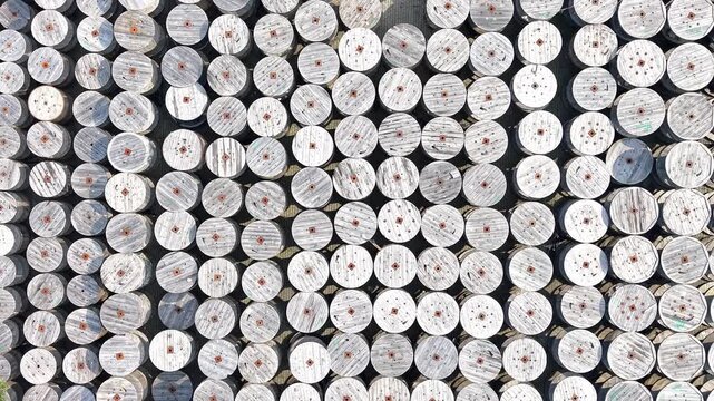 Aerial view of a warehouse displaying a large arrangement of wooden cable reels organized in rows, showcasing a systematic layout across the expansive concrete surface. Industrial place
