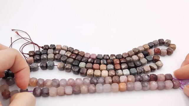 Faceted cube shaped natural gemstone beads in soft pink and purple tones arranged in matching strands on a flat white surface for jewelry design and crafting