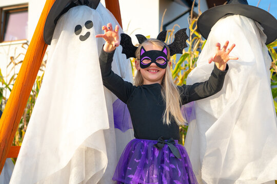Child in Halloween costume standing between two ghost decorations