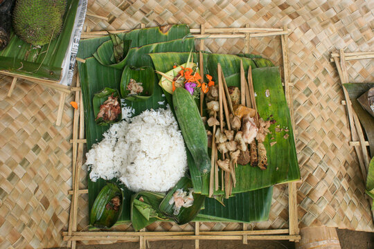 Overhead view of a ritual food offering of white rice and grilled meat skewers and a cucumber on banana leaves, Ubud, Indonesia