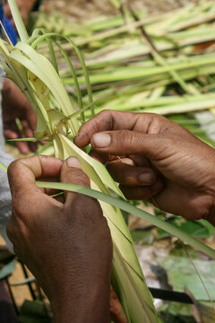 Close-up of hands braiding a palm leaf offering with strips of green leaf around them in preparation for the ceremony, Ubud, Indonesia