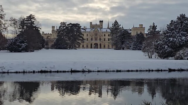Lednice Castle in winter across lake with snow and water reflections