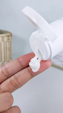 POV pouring white cream from product packaging onto index fingertip. Close up skincare application, thick moisturizing texture for daily beauty routine.