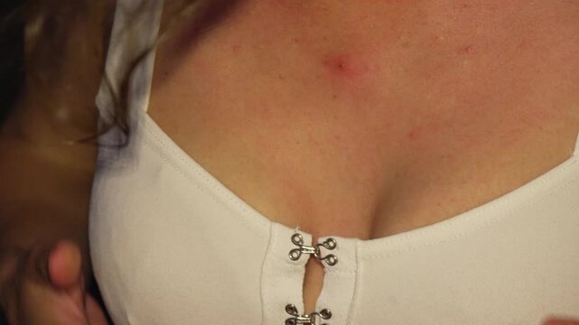 White top bodice detailed with silver hook closures worn by a woman adjusting her neckline during an evening social event. Extreme close-up shot.