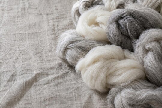 Soft white, gray wool roving fibers on rumpled linen cloth, raw unspun wool for felting, spinning crafts, nobody