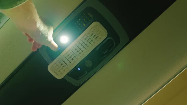 Male hand turning on ceiling light in bus interior. Overhead autonomous lighting unit with bright lamp and control panel. Public transport cabin equipment with emergency illumination system