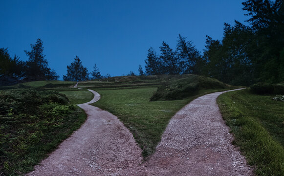 Two dirt paths diverging at dusk representing life choice and decision concept.