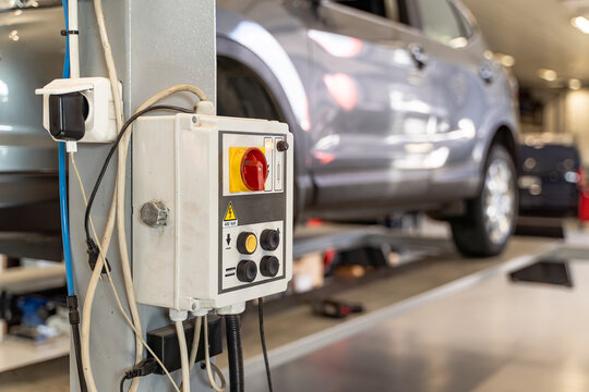Control panel of a vehicle lift with red main isolator switch, push buttons and 400 volt high voltage warning sign in a car workshop