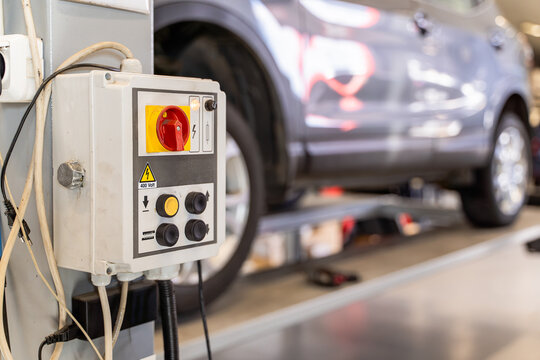 Control panel of a vehicle lift with red main isolator switch, push buttons and 400 volt high voltage warning sign in a car workshop