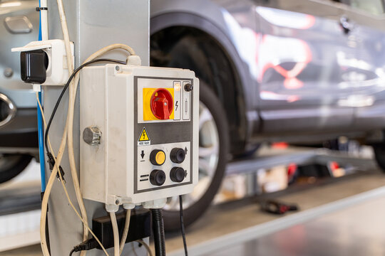 Control panel of a vehicle lift with red main isolator switch, push buttons and 400 volt high voltage warning sign in a car workshop