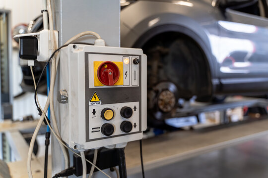 Control panel of a vehicle lift with red main isolator switch, push buttons and 400 volt high voltage warning sign in a car workshop
