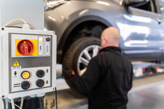 Lift control panel with red isolator switch, push buttons and 400 volt warning sign, mechanic changing a car wheel blurred in the background