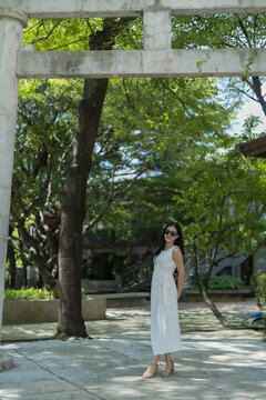 Woman in white dress standing under archway, smiling outdoors