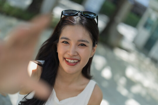 Smiling Asian woman reaching out, expressing happiness and connection outdoors