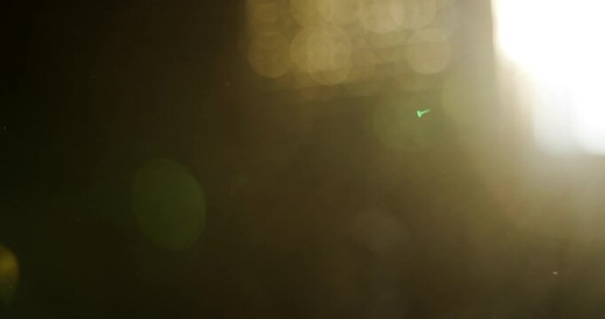 Abstract sunlight shining through a dark atmospheric scene with warm golden lens flare, glowing particles and soft bokeh. Minimal background for light, energy and illumination concepts. 4K.