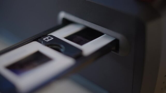 Close-up of an empty film scanner as a slide holder is inserted and then pushed through frame by frame. The manual handling of digitising analog slides, a detail of film archiving at home, Germany.