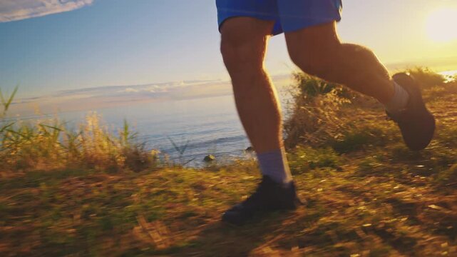 A person in blue shorts and black shoes jogs along a grassy path by a sunlit lake, emphasizing their stride against a serene backdrop.