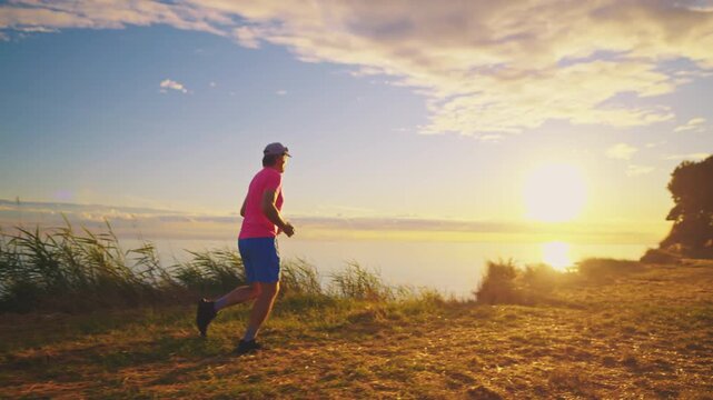 A senior adult male jogs along a lakeside trail at sunrise, the warm glow of the sun highlighting his determined stride. The serene environment and his steady pace emphasize.