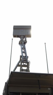 Vertical screen Military radar antenna rises above a mobile surveillance vehicle against intense sunlight with bright lens flare highlighting modern airspace monitoring technology