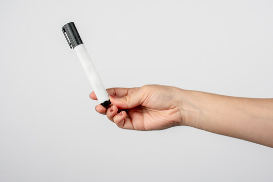 A hand is holding a white marker pen with a black cap against on white background.