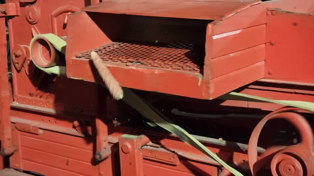 SLOW MOTION: Antique red machine automatically separating corn kernels from cobs during the harvest season, with the grain falling into a wooden crate while empty cobs collect in another