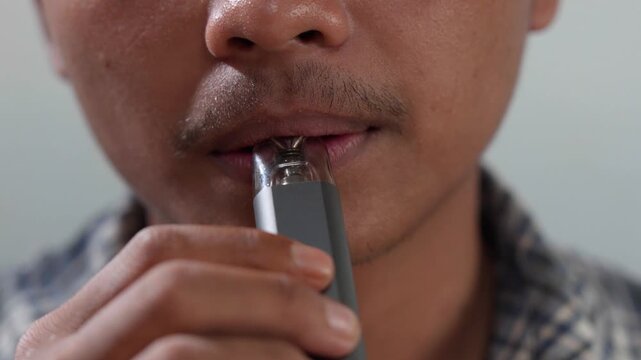 Close up of a young Asian man is smoking using vape device or electric cigarette.