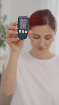 Vertical Screen: A woman holds up a glucometer showing a blood sugar level of 136 mg dL. This reading indicates a high glucose level that may concern people with diabetes.