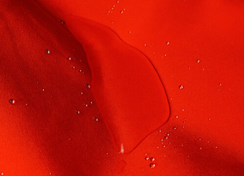 Macro shot of raindrops on vibrant red hydrophobic fabric surface close-up